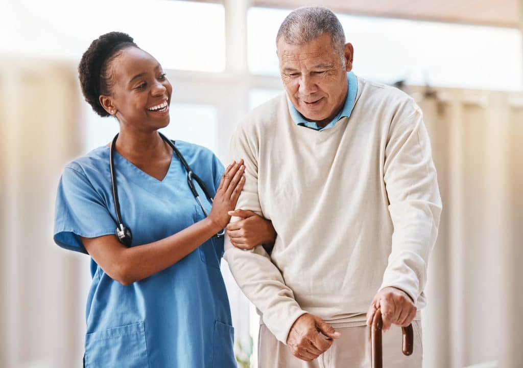 A doctor in blue scrubs helping an elderly man with physical therapy.