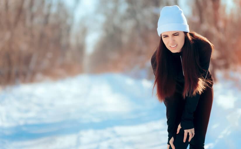 A woman out in the snow holding her knee in pain due to cold weather aches.